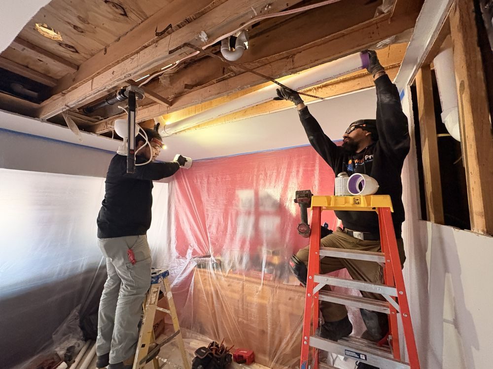 Two SwiftPro technicians in branded shirts running ductwork in a Northern Virginia home, the kind of crew that installs an Air Scrubber